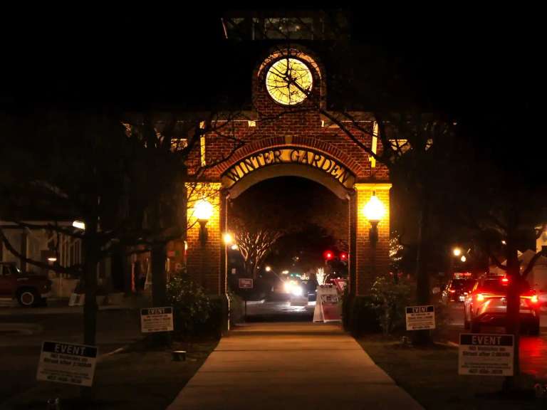The lit brick clock arch reading Winter Garden over a walkway in the historic downtown at night