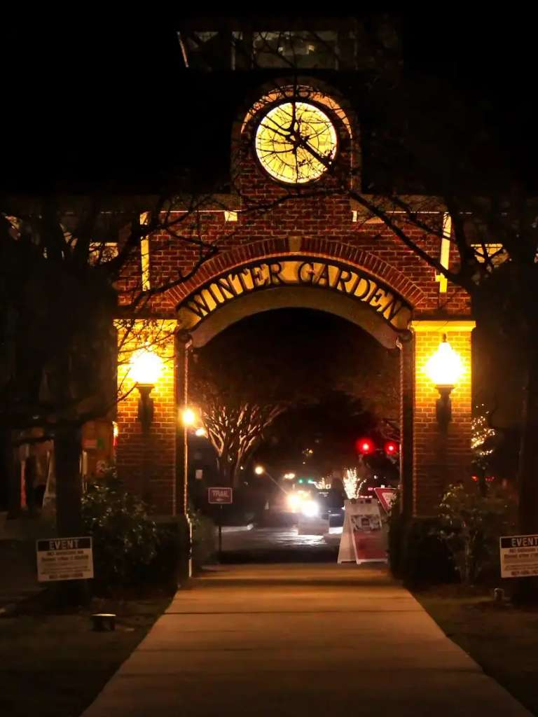 El arco de ladrillo iluminado con reloj y el nombre Winter Garden sobre un paseo del centro histórico, de noche